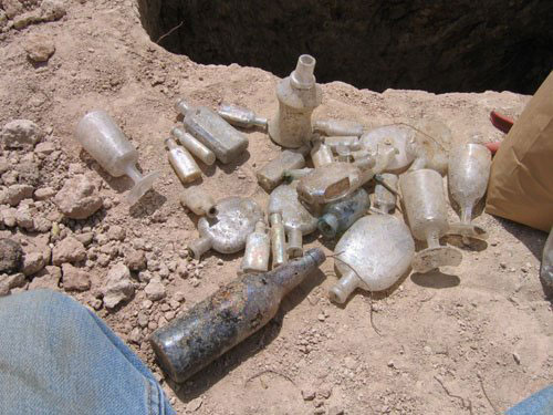 A pile of bottles and other glassware sits on the ground after being recovered from an outhouse pit by archaeologists.