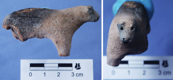 A fired-clay figurine depicts a four-legged animal. Eyes and nostrils are represented by small holes poked in the face. It has short, pointed ears and a short tail.
