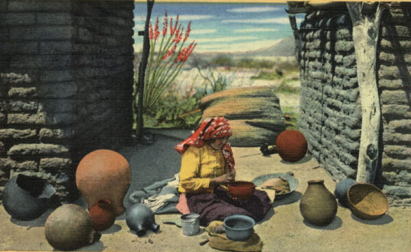 A postcard photograph shows a Tohono O'odham woman making a ceramic bowl. She is seated on the ground between two adobe buildings, wearing a yellow shirt and a red headscarf. She is surrounded by numerous clay vessels of various designs, sizes, and colors. 