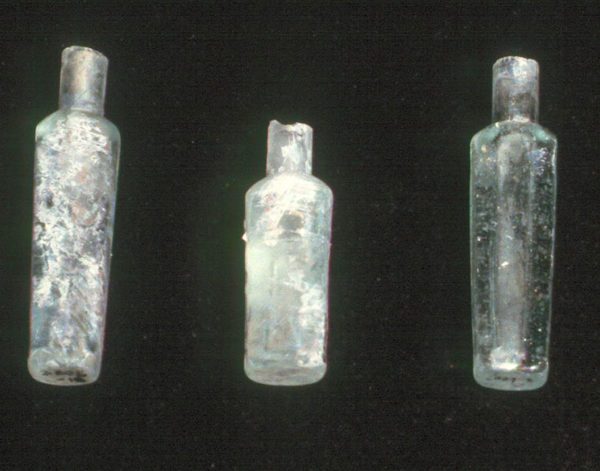 Photo of three glass Chinese medicine bottles. The bottles are relatively narrow, tall, and rectangular. They are heavily patinated.
