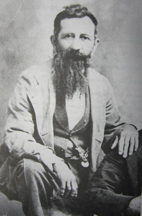 Photo of George O. Hand, diarist, Civil War soldier, corn stealer, saloon keeper, and janitor. He has a long scraggly beard and short dark hair. He is wearing a light suit jacket over a dark waistcoat and white shirt, A pocketwatch chain is visible on one side of the waistcoat.