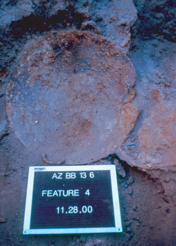 Photo of the iron wok found in Feature 4. It is a rusty brown circle.